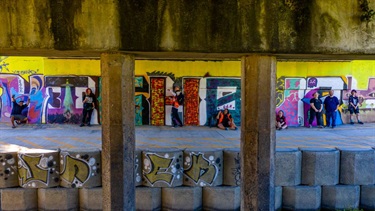 Artists painting a mural under a concrete bridge.