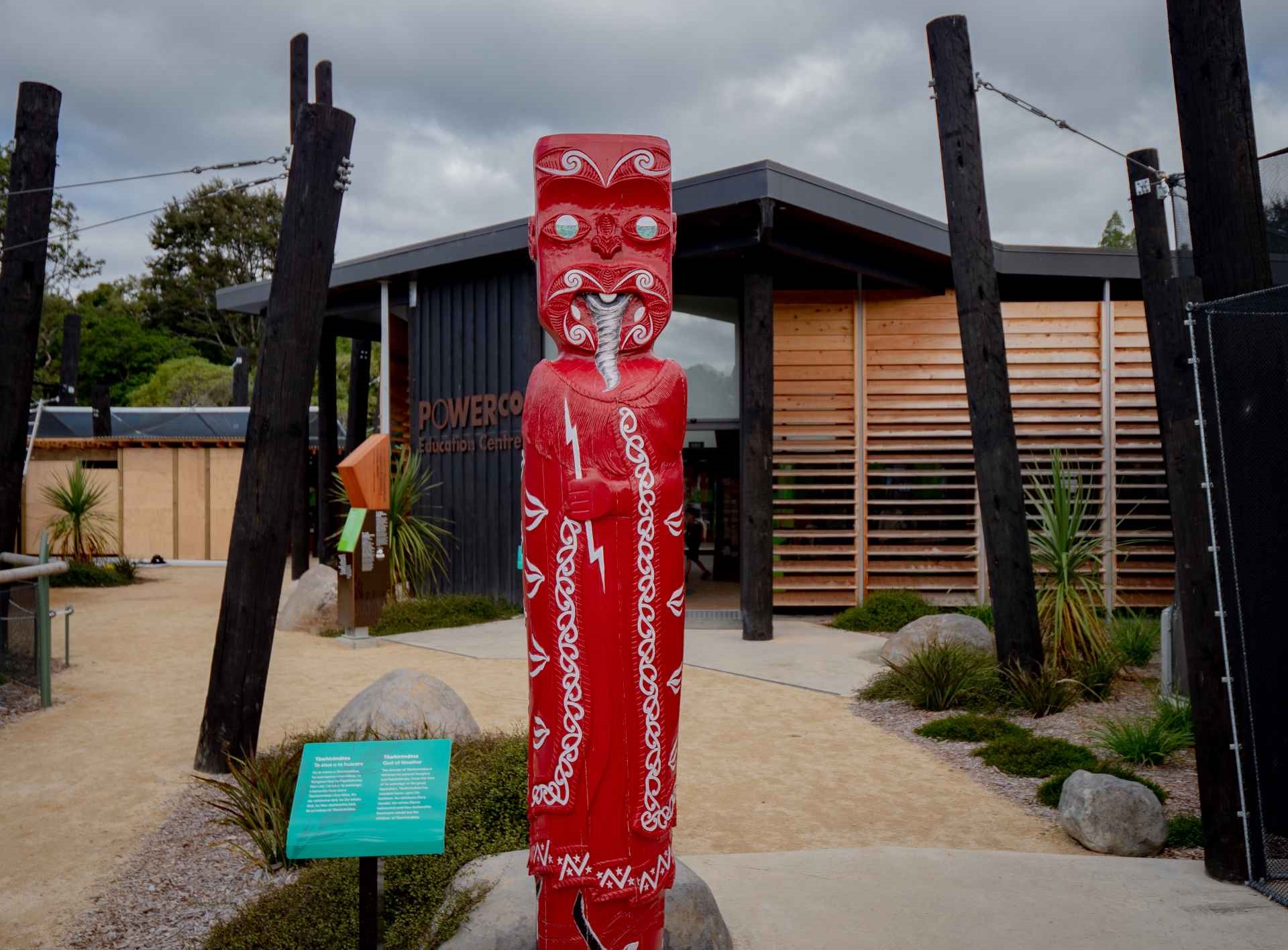 A painted pou on a path leading to the aviaries, flanked by boulders, native grasses and flax.