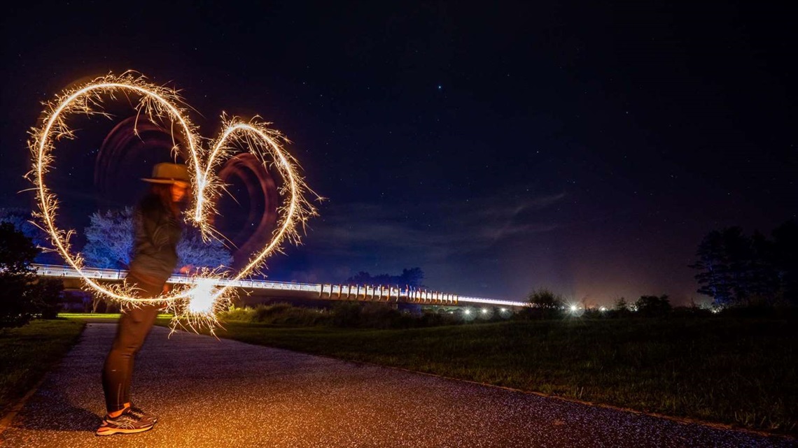 A love heart drawn with a sparkler is silhouetted against a starry night sky.