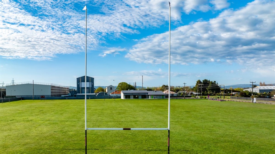 Sportsground with rugby posts and the community centre in the background.