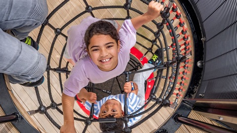 Smiling tamariki clamber up a rope tunnel.