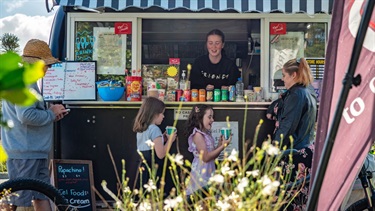 A family buying treats from a coffee cart in a city park.