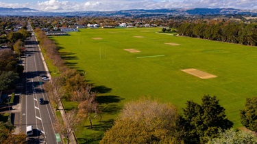 Lush green turf is punctuated by goalposts and surrounded by trees.