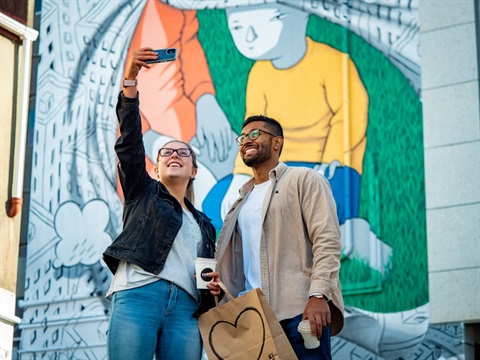 Young couple taking a selfie in front of a colourful mural.