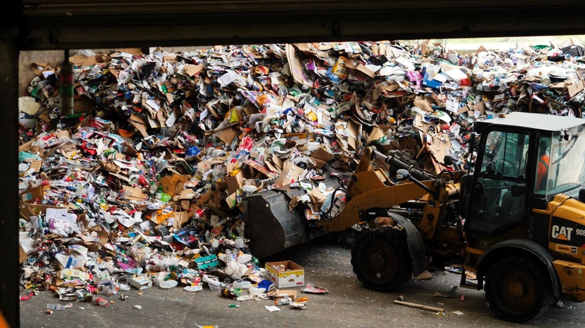 Worker dressed in hi-vis and ear-muffs operating gathering up piles of cardboard and plastics at our Awapuni resource recovery facility.