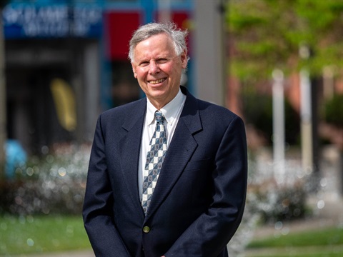 Image shows a man in suite standing in front of the fountain.