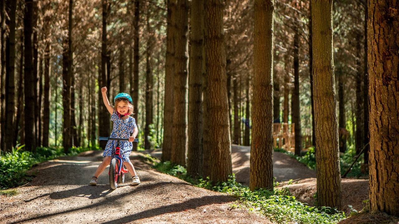 Smiling girl pumping her fist in the air as she negotiates the pump track on her balance bike.