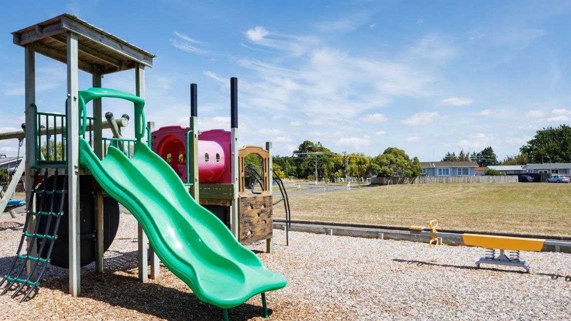 Playground with a cool tractor-themed slide nestled in the corner of a small neighbourhood reserve.