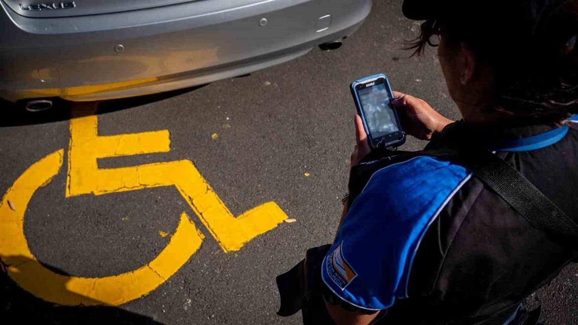 Parking officer issuing a ticket to a car illegally parked in a mobility parking space.