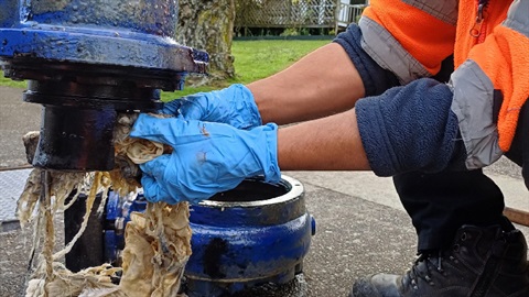 Image shows worker pulling wet tissues out from a pipe