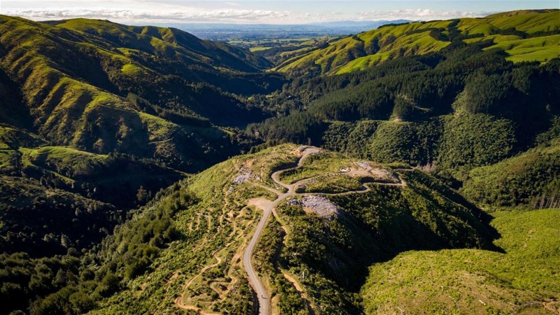 Aerial view of people mountain biking on a hill track surrounded by mountains.