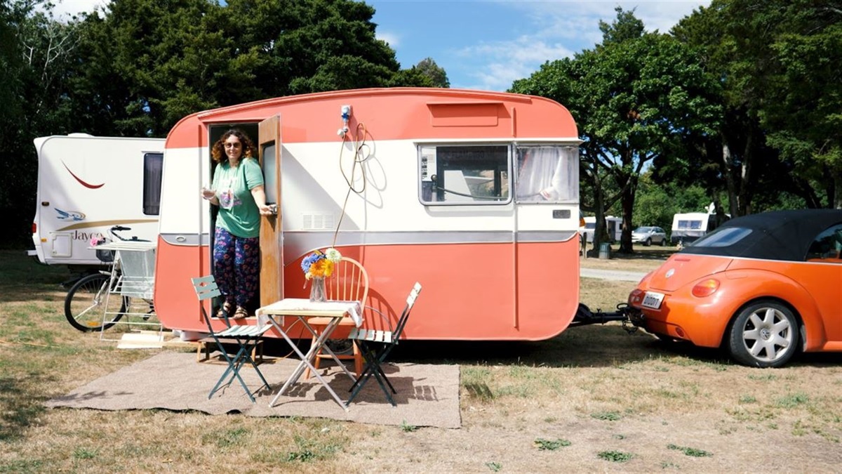 Campground set among trees at the Domain. There's a cute retro caravan in the foreground parked up next to matching car.