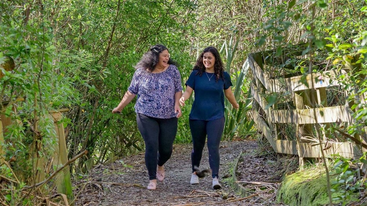 Two laughing young women in fitness gear striding along a gravel track through the bush.