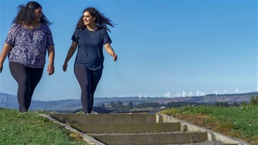 Two young women in activewear about to head down steep wood and gravel steps on a hilltop track.