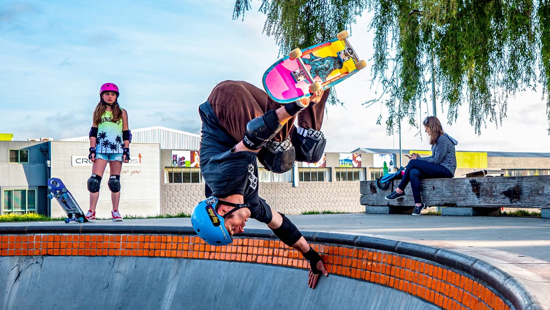 Skateboarding kid hanging upside down on the rim of the skate bowl, mid-leap.